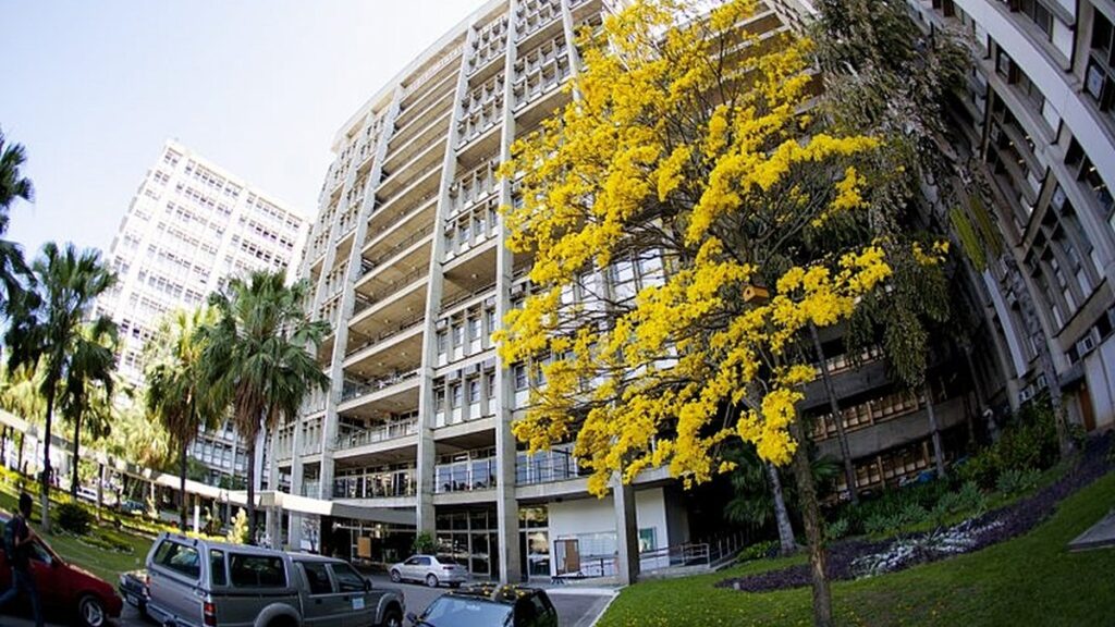 Fachada do campus da Universidade do Estado do Rio de Janeiro, com céu claro e vegetação ao redor.